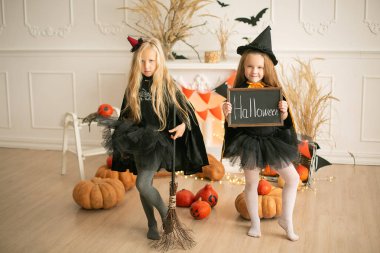 Cadılar Bayramı için cadılar bayramı kostümlü iki kız, dekor arka planında, ellerinde bir balkabağı, uzun saçlı, Avrupa tarzı sarışınlar.