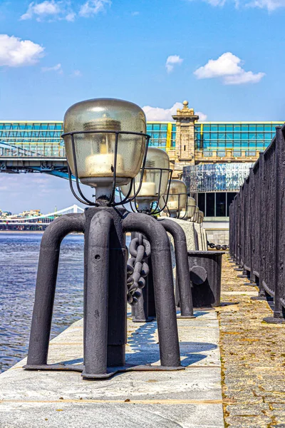A row of street lights with glass caps, on the embankment of the Moscow river, against the background of a pedestrian bridge and blue sky