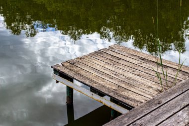 Gölde balık tutmak için küçük tahta köprü. Göldeki ağaçların yansıması.