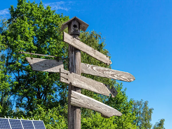 Wooden signpost with wooden arrows in the city Park, against the background of green trees, blue sky and solar panel