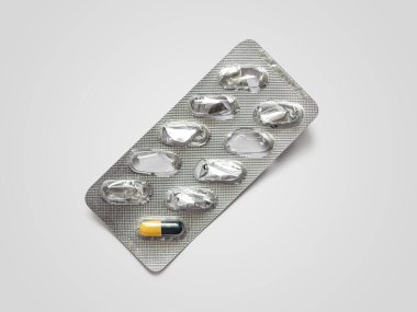 Kullanılmış ilaç paketi, folyodan yapılmış, tek bir siyah-sarı kapsül, açık arkaplanda.