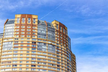 Büyük, açık kahverengi yuvarlak bir gökdelen mavi gökyüzüne karşı geçen bir uçağın yoğunlaşma izi.