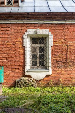 Eski bir tuğladan evin güneş ışığıyla aydınlatılmış penceresi. Evin önündeki yeşil çimenler.