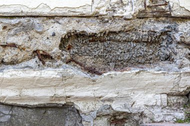 Çatlak ve çökmüş alçıyla eski gri bir duvar, beton harçla kaplı paslı demir tel.