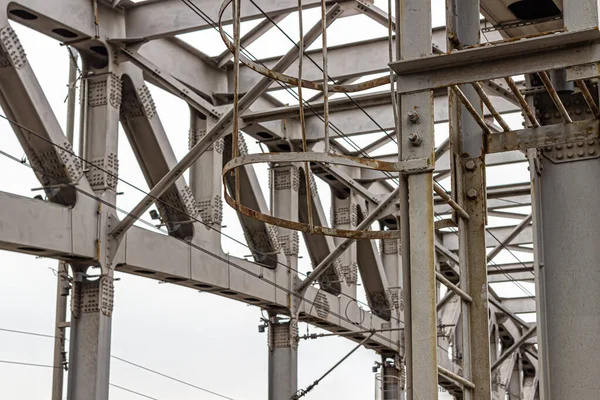 Arch of the metal structure of the railway bridge with many powerful bolts and nuts, against the gray sky
