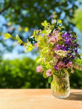 Ahşap bir yüzey üzerinde kristal dekoratif vazoda duran parlak kır çiçekleri. Bulanık çiçek arkaplanı. Boş alan.