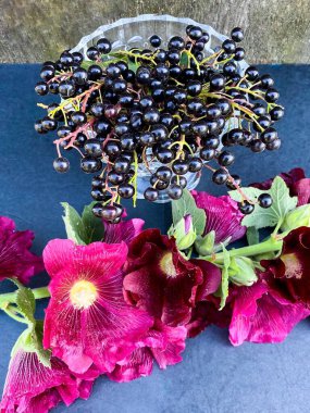 Koyu ahşap arka planda bir buket çiçekle kristal bir kasede kuş kirazının olgun kara meyveleri. Boş yer.