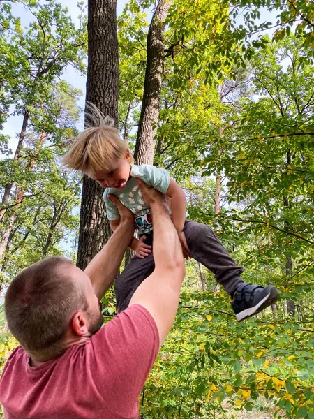 Light-skinned man lifts up cheerful little child. Concept of father-son relationship, active lifestyle.