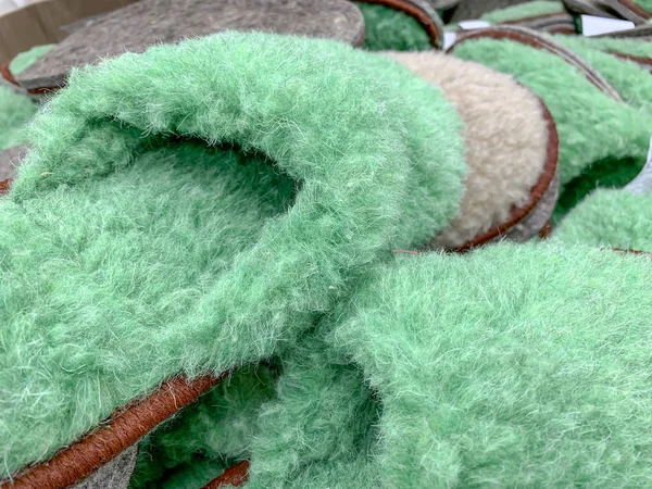 Many green fluffy fuzzy home slippers in a shop, shopping for comfort cozy home