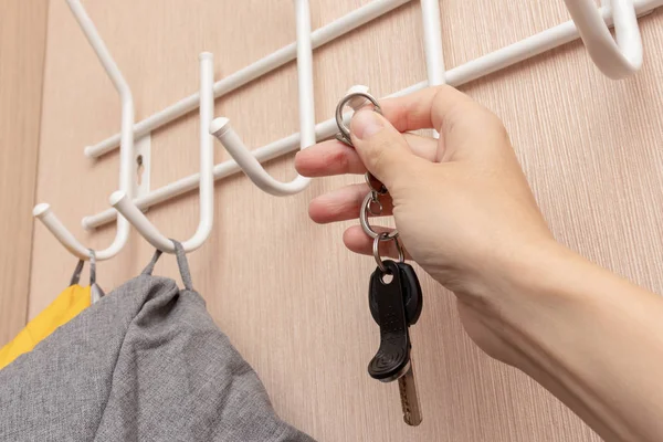 Woman hand hanging keys on a ring on a coat rack hook in a hallway, anteroom at home, home safety and security concept