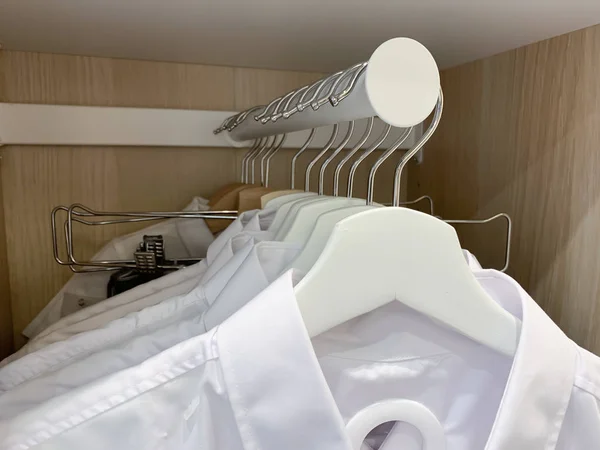 Mnoho bavlněných neformálních pánských košil visících ve skříni na bílých dřevěných ramínkách — Stock fotografie