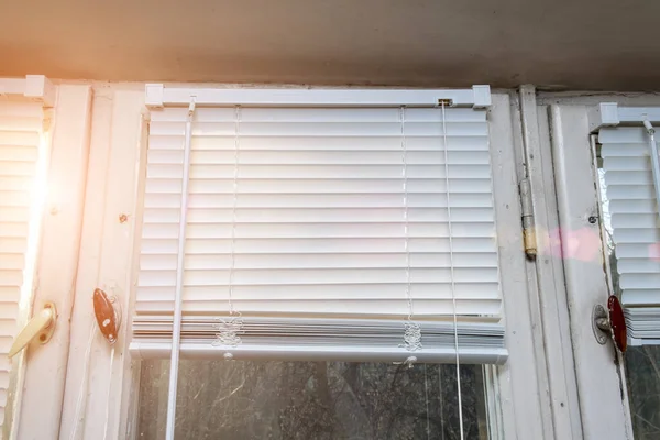 Відкриті білі алюмінієві горизонтальні віконні жалюзі на старому дерев'яному вікні як захист від сонячних променів у сонячний літній день — стокове фото