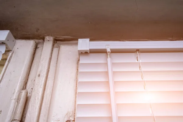 Закриті білі алюмінієві горизонтальні віконні жалюзі на старому дерев'яному вікні як захист від сонячних променів у сонячний літній день — стокове фото