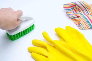 Sarı lastik eldivenler, beyaz yüzeyde duran mikrofiber mendil ve fırça, temizlik ve ev işi konsepti, ev hijyeni ve hijyenik koruma ile temizleyen bir el.