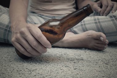Evde yerde oturan bir kadın ve alkollü içkiler, kadın alkol bağımlılığı konsepti. Boş bira bittle yakın çekim