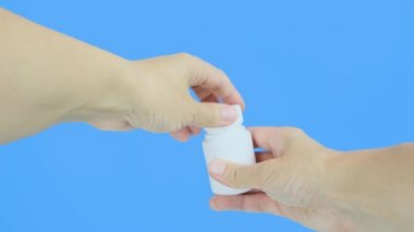 Kadın eli beyaz plastik bir kap açıyor. C vitamini drenajlı. Eline de haplar dökülüyor.