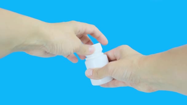 Las manos femeninas abren un recipiente de plástico blanco con vitamina c dragee y vierten pastillas en una mano, la palma contra el fondo azul — Vídeos de Stock