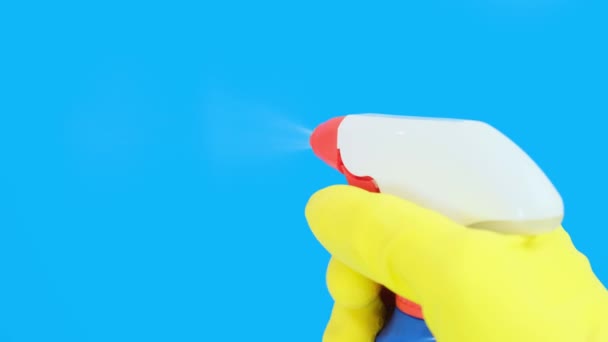Ręka w żółtej gumowej rękawicy trzymając niebieską butelkę sprayu do czyszczenia blisko i za pomocą go, niebieskie tło. Mycie, czyszczenie i wycieranie, widok z bliska — Wideo stockowe