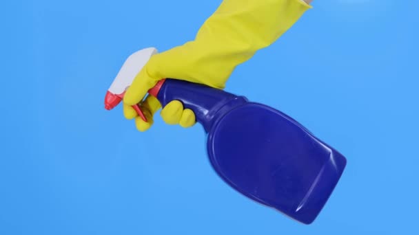 Hand in Hand ein gelber Gummihandschuh, der eine blaue Reinigungssprayflasche in Nahaufnahme hält und benutzt, blauer Hintergrund. Wasch-, Reinigungs- und Wischkonzept — Stockvideo