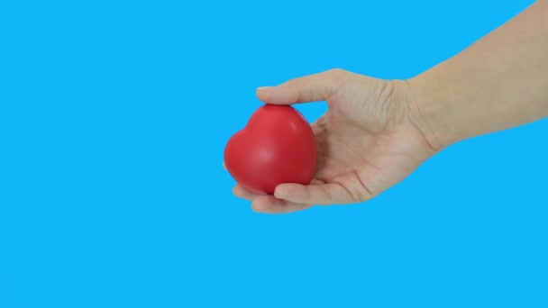 Рука тримає червоне серце на синьому фоні, здоров'я, медицину та благодійну концепцію — стокове відео