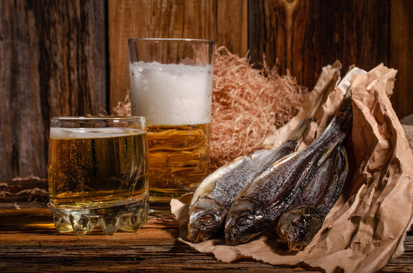 Beer in a glass next to dried fish on a wooden background