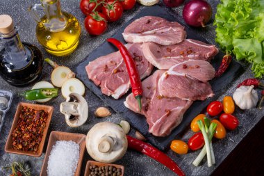 Taşta domuz bifteği, taze sebzeler, yukarıdan dokulu arka planda yakın plan pişirmek için baharatlar.