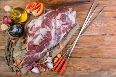 Kebap pişiriyorum. Kemiğin üzerinde çiğ kuzu budu, soğan, sarımsak, biber, terbiye ve et için şiş, ahşap bir masada. Yakın plan koyun eti. Taze koyun eti. Yukarıdan görünüşü.