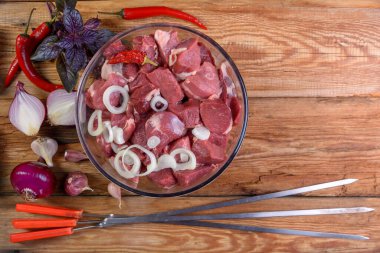 Kebap pişirmek. Kemiksiz kuzu bifteği. Parçalara ayrılmış, cam kasede et. Tahta bir masada soğan, sarımsak, biber, fesleğen ve et için şiş. Koyun eti. Kuzu şiş kebap. Yukarıdan manzara. Kırsal stil. Makro.