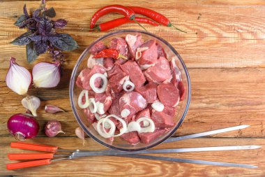 Kebap pişirmek. Kemiksiz kuzu bifteği. Parçalara ayrılmış, cam kasede et. Tahta bir masada soğan, sarımsak, biber, fesleğen ve et için şiş. Koyun eti. Kuzu şiş kebap. Yukarıdan manzara. Kırsal stil. Makro.