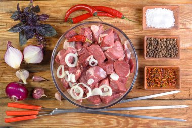 Kebap pişirmek. Kemiksiz kuzu bifteği. Parçalara ayrılmış, cam kasede et. Tahta bir masada soğan, sarımsak, biber, fesleğen ve et için şiş. Koyun eti. Kuzu şiş kebap. Yukarıdan manzara. Kırsal stil. Makro.