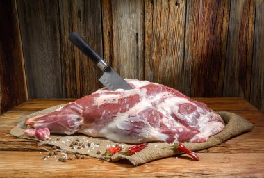 Ahşap bir masanın üzerinde mutfaktaki bıçakla delinmiş bir koyun eti bacağı yatar. Baharatlı koyun eti, yakından. Taze koyun eti. Yatay görüş. Rustik stil..