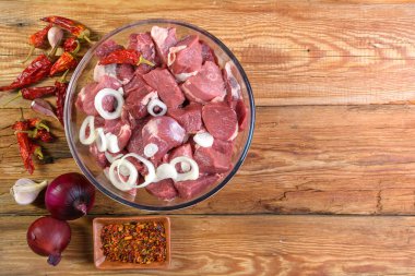 Kemiksiz kuzu eti, dilimlenmiş ve soğanla marine edilmiş, cam kasede et, fesleğen, acı biber, ahşap masada terbiye, üst manzara, yakın çekim. makro