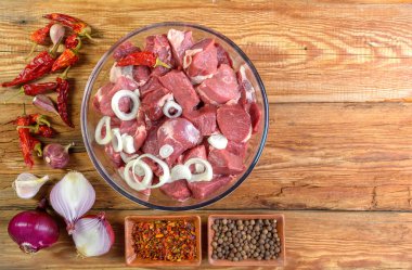 Kemiksiz kuzu bifteği, dilimlenmiş ve soğanla marine edilmiş, cam kasede et, fesleğen, acı biber, ahşap masada terbiye, üst manzara, yakın çekim, seçici odaklanma.