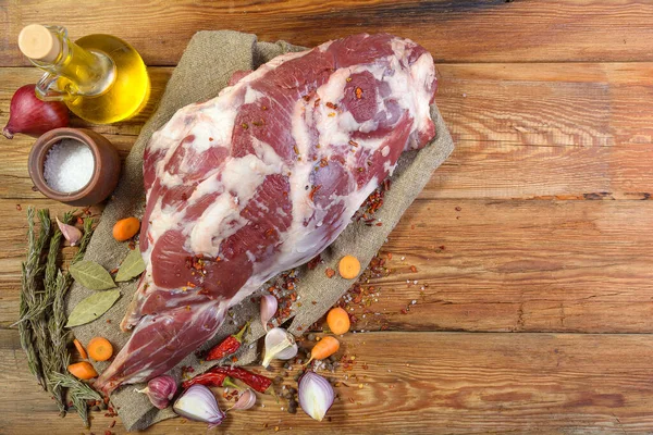 Çuval bezi, soğan, sarımsak, biber, tuz, biberiye ve sebze yağının üzerine işlenmemiş bir koyun bacağı. Yakın plan koyun eti. Taze koyun eti. Yukarıdan görünüşü.