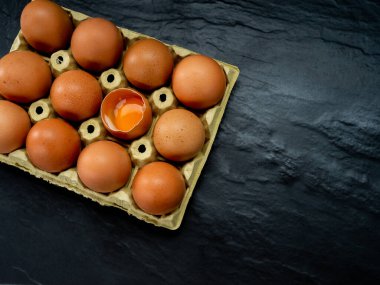 Siyah arka planda sarı karton yumurta kabı içinde yumurtalar.