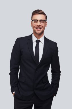 elleri ceplerinde tutmak ve gri arka plan karşı dururken gülümseme ile kameraya bakarak tam takım yakışıklı genç adam