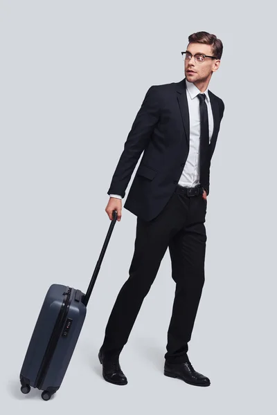 スーツケースは 灰色の背景に対して立っている間よそ見と良い探している若い男の完全な長さ — ストック写真