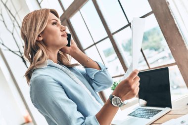 cep telefonu üzerinde konuşurken, kağıt belge basılı tutup pencereden bakıyor güzel sarışın kadın 