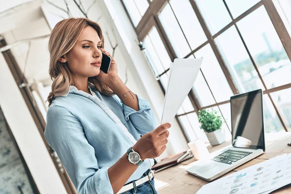 Allvarlig Blond Kvinna Talar Mobiltelefon Och Läsa Pappersdokument — Stockfoto