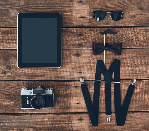 düz dijital tablet, fotoğraf makinesi, jartiyer, pervane, papyon ve ahşap masanın üzerinde yatan gözlük çekim yatıyordu