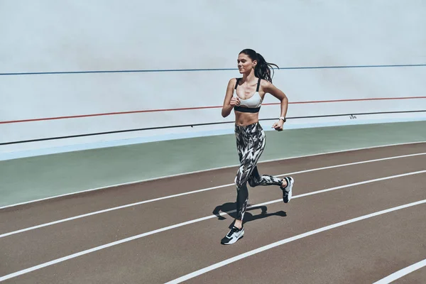 sportive smiling woman in leggings jogging on stadium