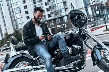Bisiklet üzerinde oturan ve cep telefonu tarama deri ceketli adamı yakışıklı genç motosikletçi 