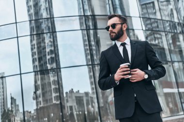 işadamı takım elbise ve açık havada cam Binası, ayakta iken tek kullanımlık Kupası tutan güneş gözlüğü 