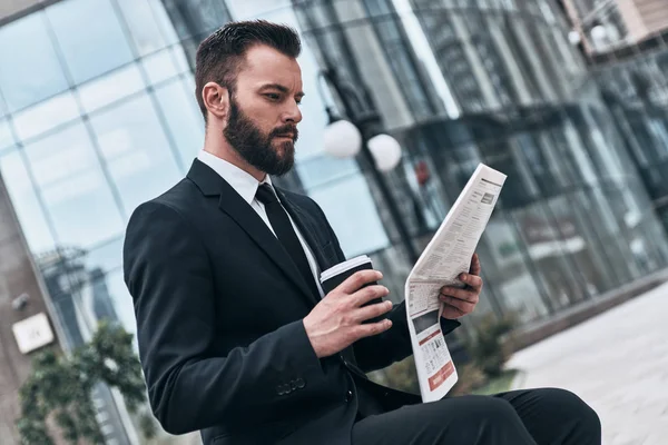 businessman in suit reading newspaper and holding coffee mug in street