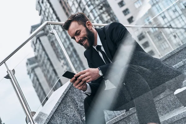 Usmívající Muž Obleku Pomocí Chytrého Telefonu Zatímco Sedí Schodech Venku — Stock fotografie