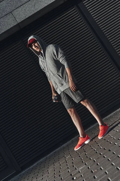 Genç adam sokakta duran ve şişe su ile tutarak giyim spor