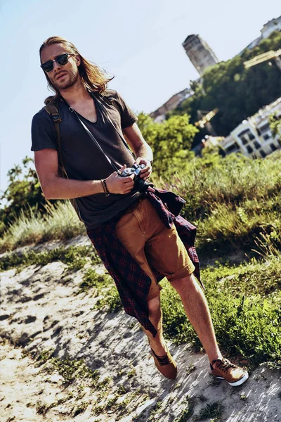 full length of young man with camera walking on hill outdoors