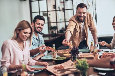akşam yemeği parti masada bira ile Pizza dilimleri çekerken gülümseyen arkadaşlar 