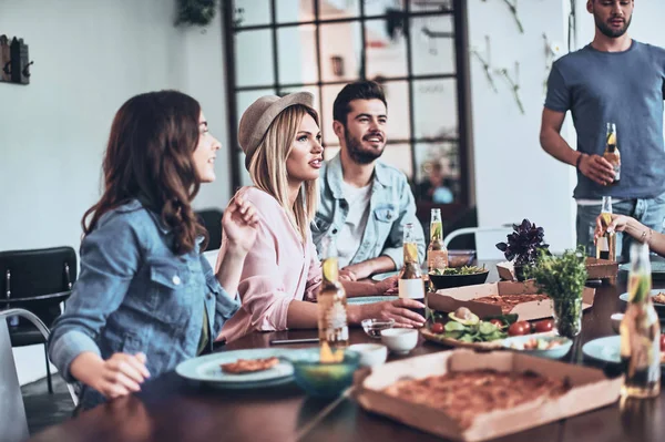 Grup Genç arkadaşlar konuşmak ve kapalı bir akşam yemeği yerken gülümseyen casual giyim