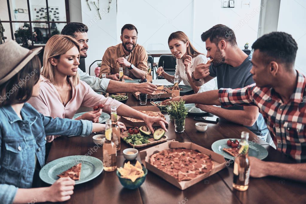 young people in casual wear eating pizza at table in restaurant 